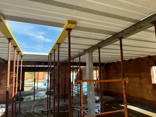 Intérieur d'un bâtiment en construction avec supports et ciel visible à travers une ouverture.