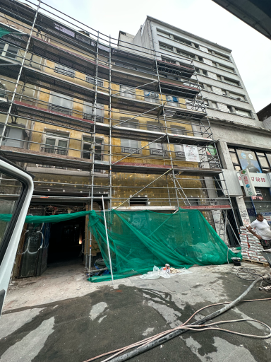 enduit projeté Façade d'immeuble en rénovation avec échafaudages et bâches vertes.